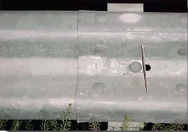 Photo. This photo is a head-on close-up view of a reflector sticking out perpendicular to the guardrail surface