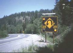 Photo.  Photo of a Speed actuated sign - the sign says SPEED TOO FAST FOR CURVE on a yellow diamond and has a rectangular advisory plaque on the post which says WHEN FLASING.  The signs are accompanied by a flashing beacon consisting of two flashing yellow LEDs placed on top.