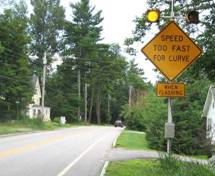 Photo.  Photo is of a flashing beacon warning sign showing a hairpin curve with 35 MPH advised speed limit.  The sign is a single piece construction with 4 embedded flashing yellow LEDs.