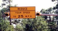 Photo.  Dynamic curve speed warning sign.  Two photos show a distant and close up of this warning sign.  The sign is on a mast arm over the roadway preceding a curve and reads, REDUCE YOUR SPEED TO 25 MPH.  It has a flashing yellow LED on each side of the sign that flashes when an approaching vehicle exceeds the advised limit.