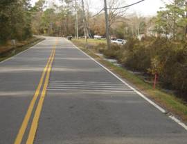 Photo.  Distant view of RRS placed 200 ft prior to a curve on a 2 lane roadway.  There are 5 sets of lines and grooves that transverse the lane which approaches the curve.