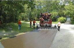 Photo.  Photo shows workers using a machine to apply a skid resistive pavement surface in a curve.