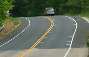 Photo.  This photo shows optical speed bars placed on a curve.  The speed bars are transverse lines which extend from the centerline and edge line into the travel lane at varying intervals.  They are placed closer together as the vehicle enters the curve, thus making a driver perceive a faster traveling speed