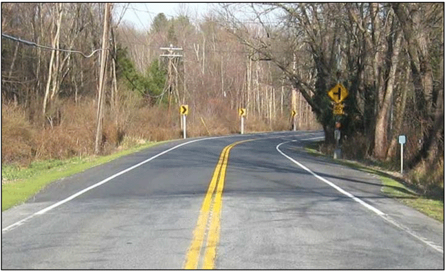 Photograph of a two-lane horizontal curve with paved shoulders on each side. Chevrons are installed on the outside of the curve. A horizontal curve warning sign is installed on the inside of the curve. Shoulders on both sides have been widened.