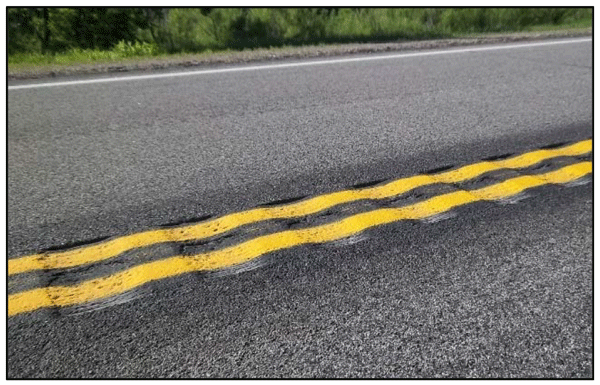Close-up photograph of milled centerline rumble strips. The rumble strips are milled over the center line of a two-lane roadway.