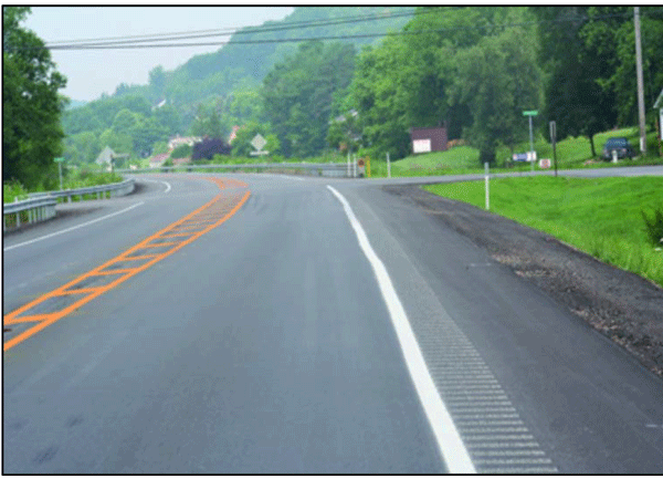 Photograph showing a combination of markings and rumble strips narrows the lane width approaching the intersections. The rumble strips are milled along the edge line. The narrowing is accomplished by gradually tapering out from the center.