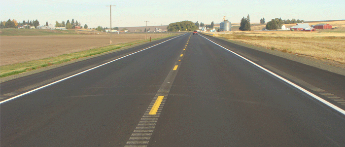 Photograph. Combination milled CLRS and SRS.  Photograph of a two-lane roadway with milled centerline rumble strips in the center and shoulder rumble strips on both sides.