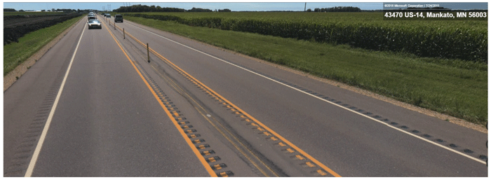 Photograph. Buffer median on Highway 14 from Bing Streetside. Photograph of a two-lane roadway with tube delineators on an eight-foot-wide buffer median. A double striped yellow line with center line rumble strips is installed on both sides of the tube delineators. The roadway also has shoulder rumble strips. 