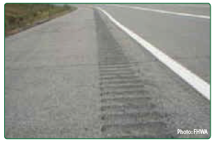 A close up of ashphalt with shoulder rumble strips milled into the surface.