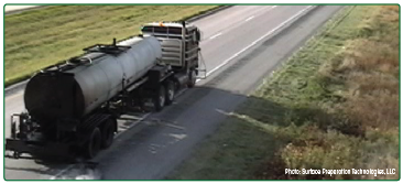 A tanker truck traveling along the edge of a roadway applying a fog seal to the edgeline rumble strip.