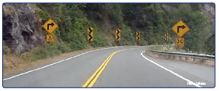 US 199 in Del Norte County on the approach to a horizontal curve with curve warning signs, chevrons, and advisory speed placards. Photo courtesy of Caltrans.