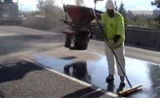A worker spreading binder across the surface of a treated lane with a broom