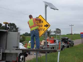 Photo of a worker mounting a new sign warning approaching vehicles to look for traffic.
