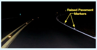 The same roadway at night  with RPMs reflecting the headlights of an oncoming vehicle.