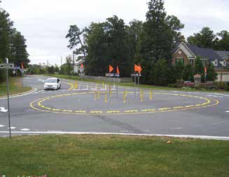 Wide shot of Virginia's "instant roundabout" showing a white car driving in the roundabout and a suburban house in the background