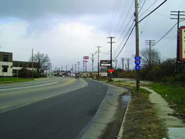 The photo shows Spring Grove Avenue: a four-lane undivided arterial road with a worn pedestrian pathway in an urban environment.