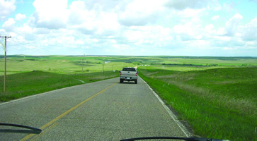 The photos shows BIA 44 west of Mahto, SD: a two lane rural road with grassy shoulders.