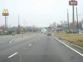 Photo shows Clear Lake Avenue, looking west toward intersection with Dirksen Parkway.  The roadway is a four-lane divided cross-section with channelized left turn bays, and commercial properties on both sides.