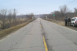 The photo shows US 60 crossing the Buck Creek bridge.  The roadway is a two-lane rural road with no shoulders and poor pavement conditions.  The RSA Team is shown at the side of the road.