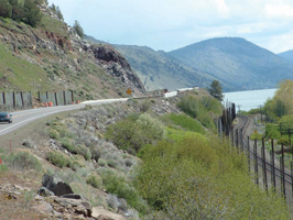 The photo shows US 97 through the audit segment.  The road is a two-lane rural road with a steep uphill embankment on one side, a steep downhill embankment on the other.  At the bottom of the embankment are a railroad and lake.