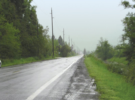 The photo shows 172nd Avenue near Ward Road: a two-lane rural road with narrow paved and gravel shoulders and a ditch on one side, in a rural environment.