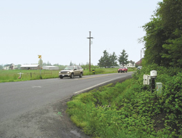 The photo shows 182nd Avenue at 119th Street: a two-lane rural road with narrow paved shoulders and a ditch on one side, in a rural environment.