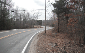 Photo of Snake Hill Road showing a curve in the road and some power lines with a utility pole in the middle of the picture.  Trees are on the right hand side.