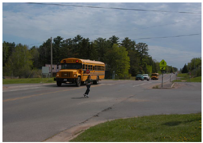 Photo of a school bus dropping off children on a rural raodway, with one child running across the roadway in front of the bus.