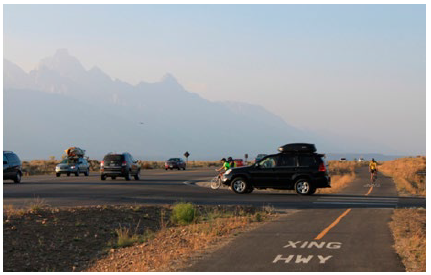 An SUV crossing a bike path at a dedicated highway crossing point to reach a highway in the Grand Tetons.