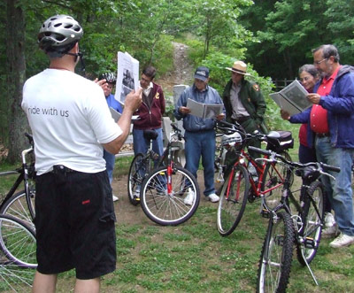 Page 22 photo: A group of dismounted cyclists reviewing trail map information led by a biking group leader, also dismounted. 