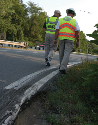Page 14 photo. This image shows two men in reflective vests walking along a roadside. Their vests indicate that one is a member of law enforcement and the other is a member of a State Department of Transportation.