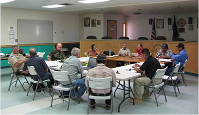 Page 8 photo. This photo shows a collection of people sitting at a group of tables having a discussion. 