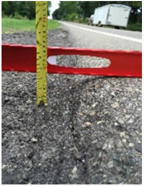 Photo shows the edge of a paved roadway with a level and ruler. The roadway has a slanted edge due to the SafetyEdge<sup>SM</sup> treatment.