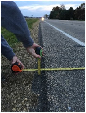 Photo shows the edge of a paved roadway with a level and ruler. The roadway has a standard edge.