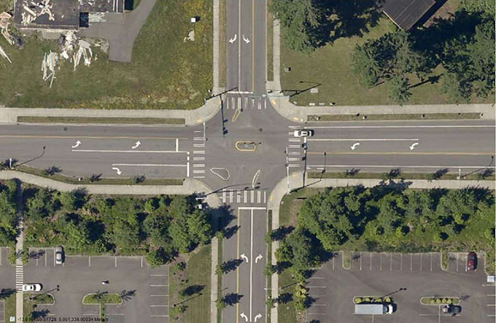 Figure 3.24.7. Forced Turn Island Blocking Side Street Through Movements and Allowing All Turns â€“ Aerial. This figure contains an aerial photograph showing a complete intersection. The left, top, and bottom legs allow left and right turns. The top and bottom legs can't be entered from opposite lanes. Cross traffic is only allowed on the street running left to right. A collection of islands are used to manage the turns.