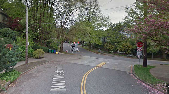 Figure 3.6.4. Corner Extension at Realigned Intersection (Reverse View). This figure contains a photograph of the same street shown in Figure 3.6.3 from a reverse view. The tree lined street curves to the right and there is a stop sign and a no left turn sign on the right corner of the street at the intersection. The street it intersects with curves from the top left of the photograph down and across the center of the photograph to the right.