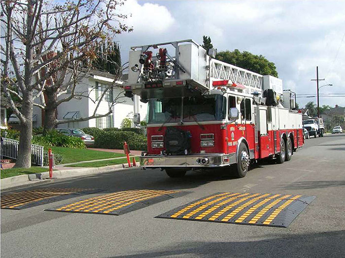 Figure 3.11.4. Fire Truck Approaching Test Speed Cushion. This figure contains a photograph of a residential street with a fire truck approaching a set of test speed cushions with yellow stripes.