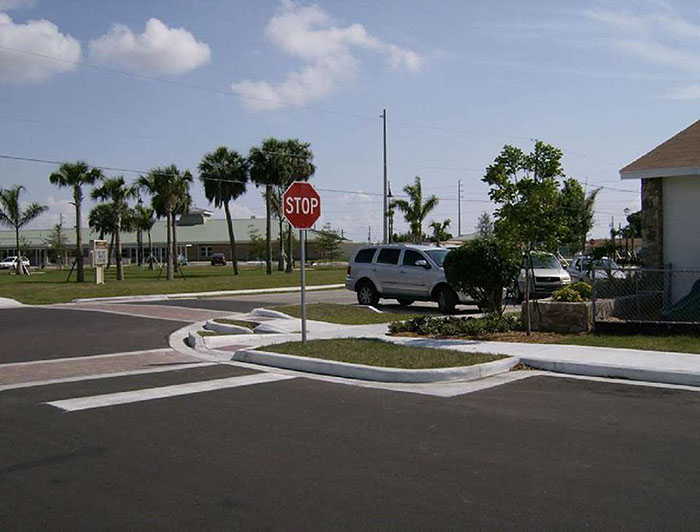 Figure 3.16.4. Corner Extension in Suburban Setting. This figures contains a photograph which shows a corner where two streets intersect. A corner extension is built out onto the street nearest the bottom of the picture. A stop sign is visible and there are several vehicles parked diagonally on the other street near the corner of a single story building. Palm trees grow in the lot opposite the house and a school can be seen in the distance.