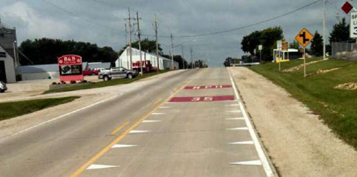 Figure 5-8 Horizontal signing at community entrance in Jesup, IA [Treatment authorized with MUTCD experimental waiver] (Image Source: Neal Hawkins). This photo shows an experimental treatment with 35 MPH painted in red on the road. Note: The red background coloring is not MUTCD compliant, and should only be installed after receiving approval from FHWA through an experimentation waiver.