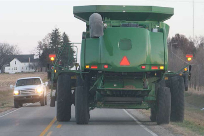 Figure 1-3 Oversized agricultural vehicle traversing the main roadway through a rural community. (Image Source: Neal Hawkins) A smaller pickup truck is attempting to pass the large oversized vehicle.
