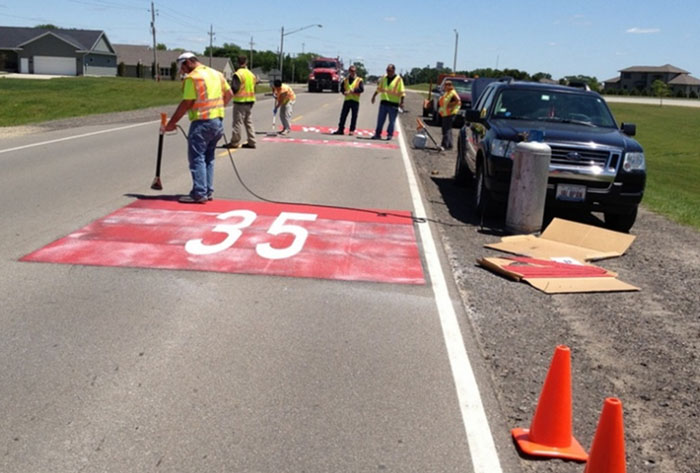 Figure 6-4 Thermoplastic pavement marking installation [Treatment authorized with MUTCD experimental waiver] (Image Source: Hallmark, et al. 2002). This photo shows an experimental treatment with 35 MPH painted in red on the road. Note: The red background coloring is not MUTCD compliant, and should only be installed after receiving approval from FHWA through an experimentation waiver. In this photo, you can see the worn red paint being retreated with thermoplastic marking to improve wear and longevity.