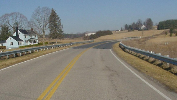 Photo. A roadway is shown at the approach to a curve. A difference can be seen in the color of the road surface in the curve.