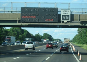 Photo of a variable Reduce Speed sign and a VSL sign mounted over one side of a divided highway.