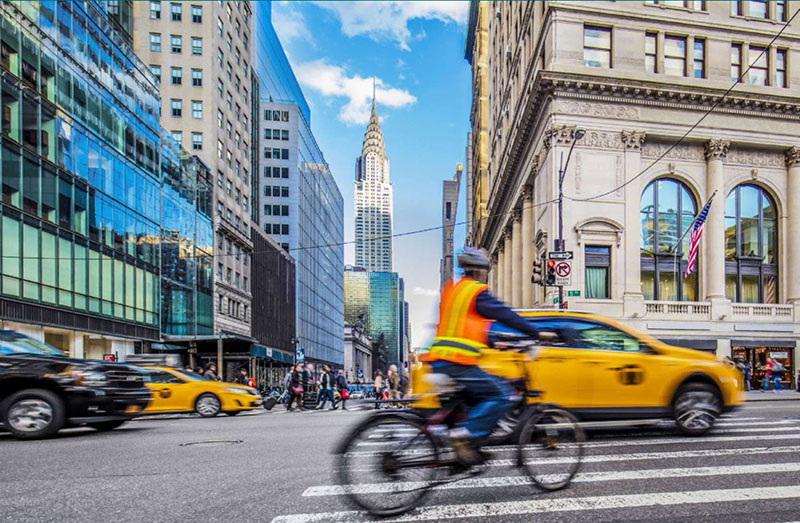 Stock art photo of a busy New York City street with cars and pedestrians in motion in an intersection with the iconic Chrysler Building in the background.