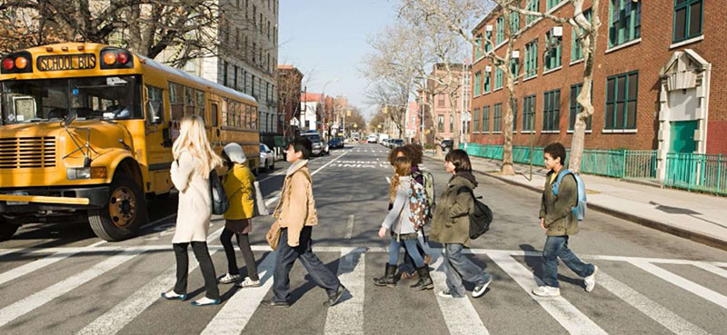 Photo of School Children crossing a street in NYC on a crosswalk in front of a stopped bus.
