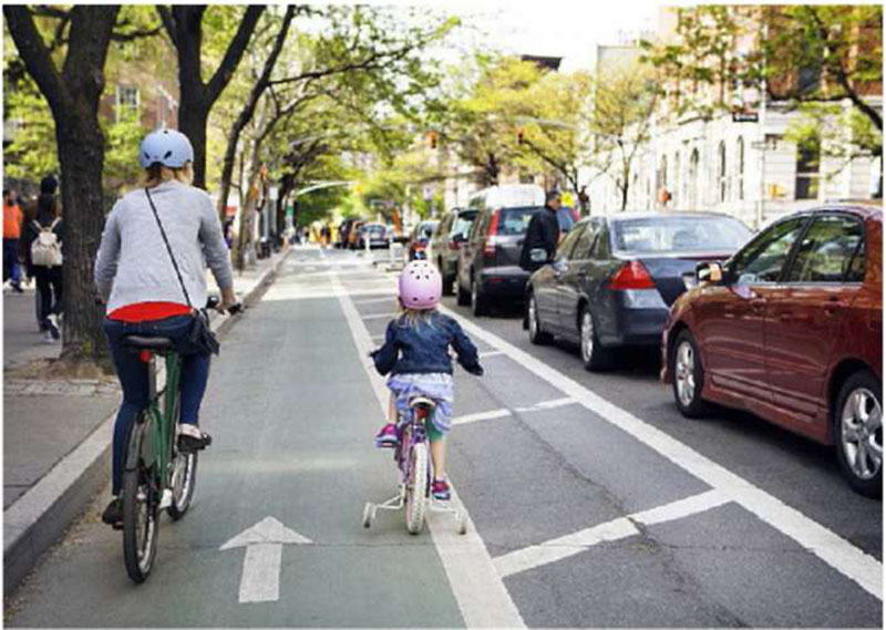 Photo of an adult and child riding in a bike lane on a busy road.