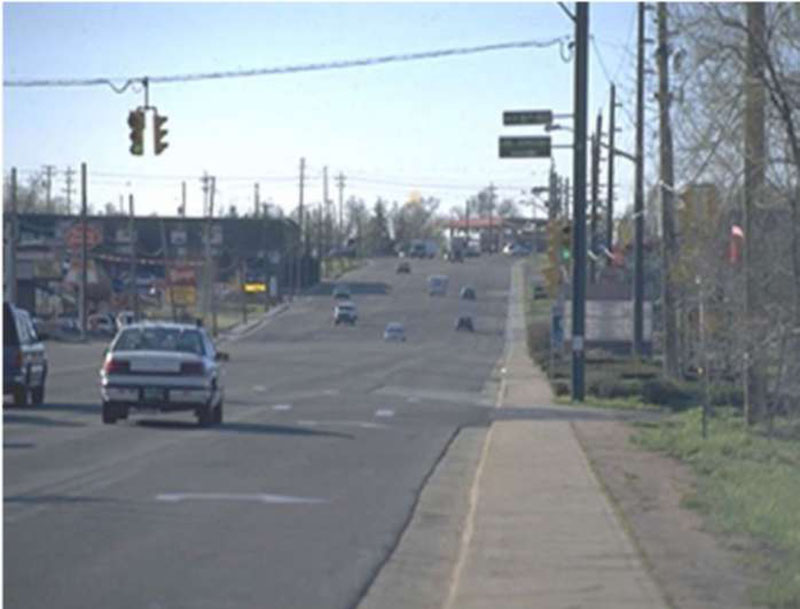 Photo of South Golden Road before improvements showing a long wide road with cars at an intersection and businesses in the distance.