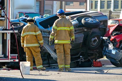 A photo of two firefighters investigating a wrecked car on its side.