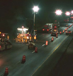 night scene of paving equipment with various powerful lighs illuminating the road surface and work vehicles
