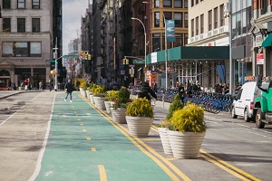 road in NYC with a green bike and pedestrian lane, with Citi Bikes racked on the right.